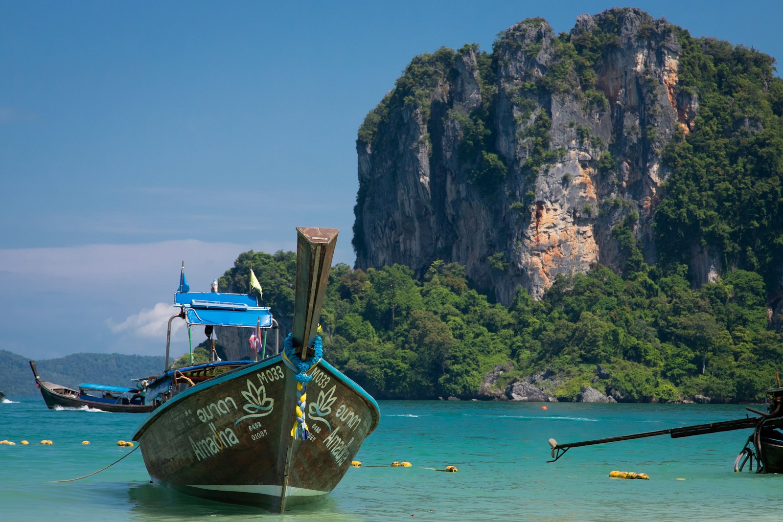 A traditional longtail boat on turquoise water beneath the limestone cliffs at Railay Beach, Krabi